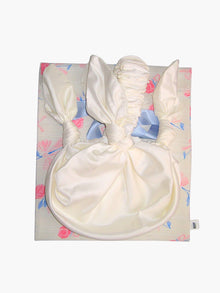 ivory bamboo silk satin knotted handbag, sat on top of a floral patterned ribbon tied fabric git pouch, set against a white background