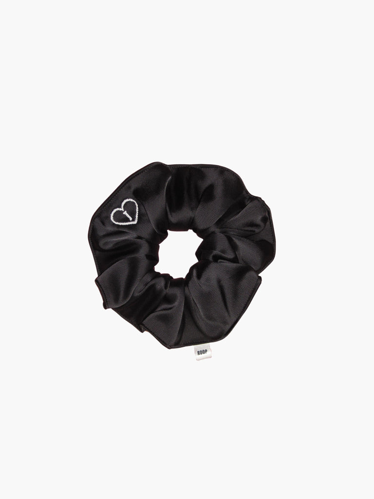 Black satin scrunchie embroidered with a white heart with the letter J inside, set on a white background