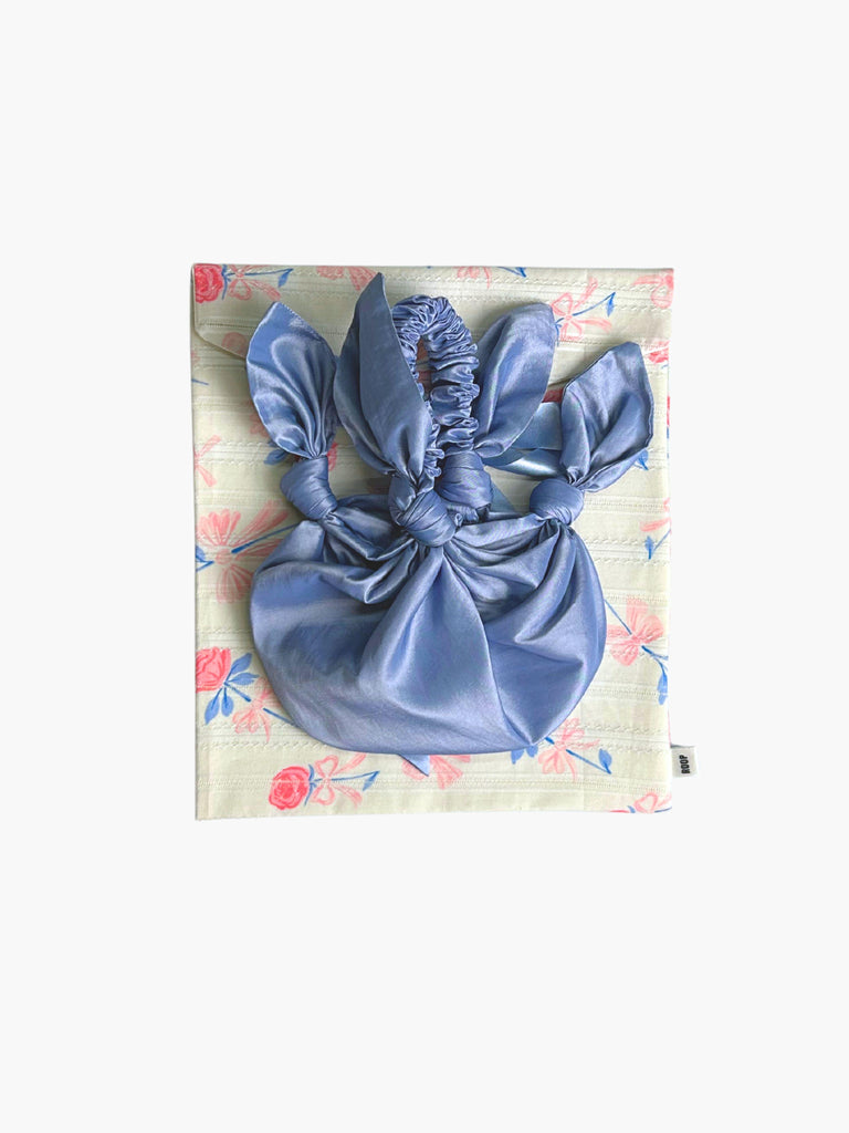 lilac taffeta knotted handbag with ruched handle, sat on top of a floral patterned ribbon tied fabric git pouch, set against a white background