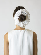 Person wearing an Ivory ruffled scrunchie over their bun with black embroidery that reads 'bride to be', set on a white background