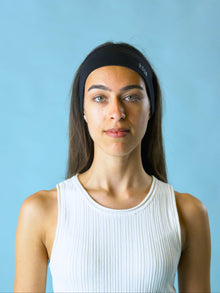 Woman wearing a black stretch headband with ROOP logo on a light blue background