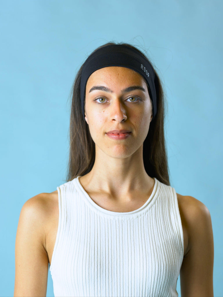 Woman wearing a black stretch headband with ROOP logo on a light blue background