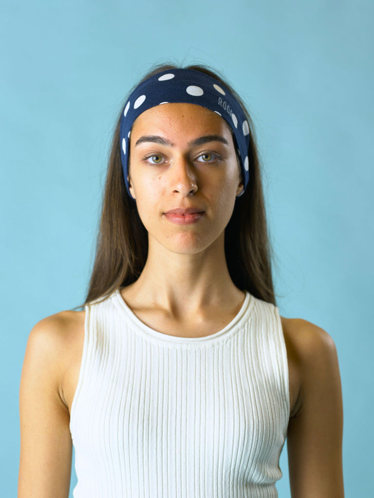 Woman wearing a navy blue stretch headband with white polka dots against a light blue background