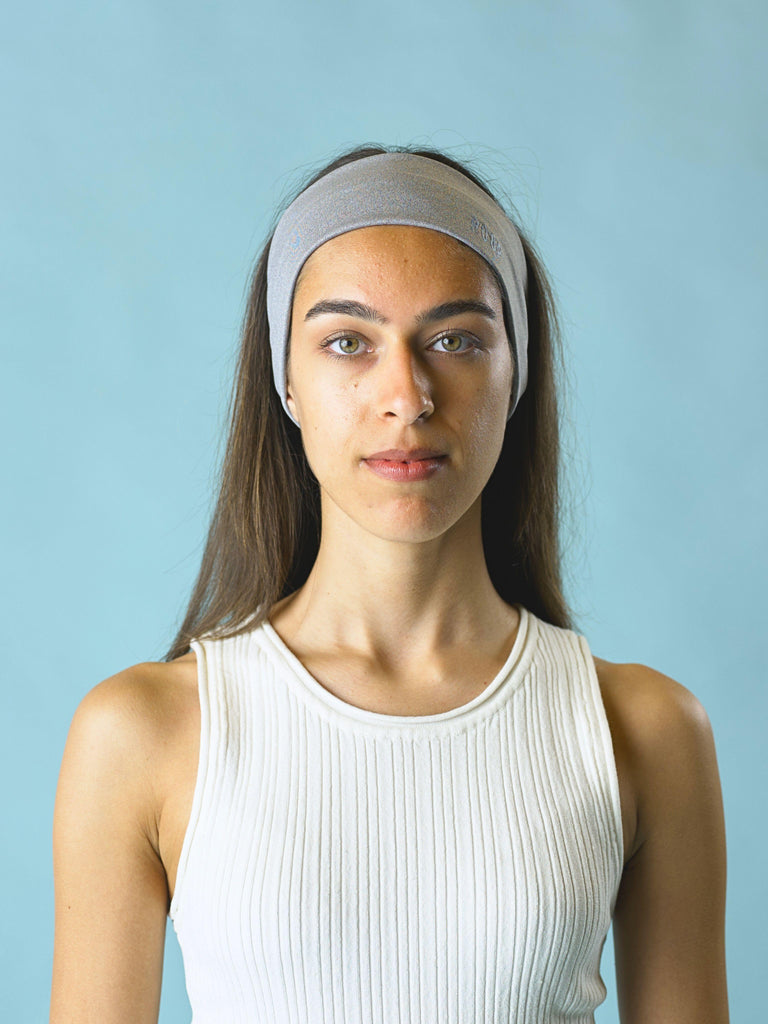 Woman wearing a grey stretch headband against a light blue background