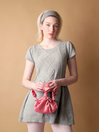 Woman wearing a gray knit dress holding a pink knotted bag against a beige background