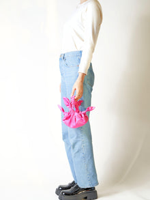 Person wearing light blue jeans holds a pink knotted bag held in hand against a white background