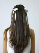 Person with long brown hair wearing two blue satin hair bow clips on a white background