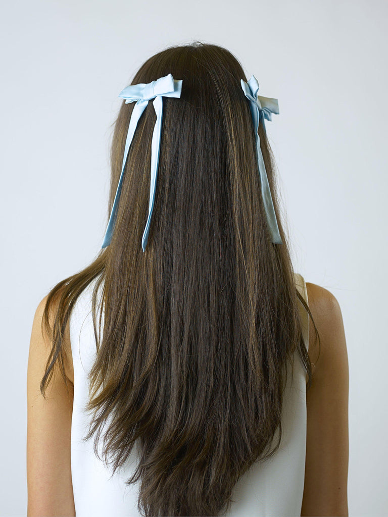 Person with long brown hair wearing two blue satin hair bow clips on a white background