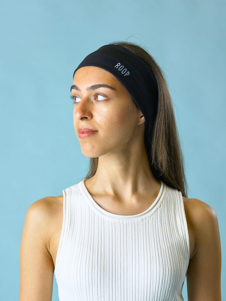 Woman wearing a cream ribbed tank top and a black headband with 'ROOP' branding against a light blue background