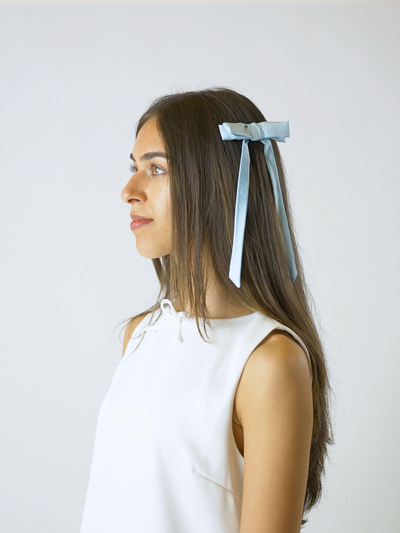 model in side profile wears an ivory sleeveless dress and a blue satin hair bow clip