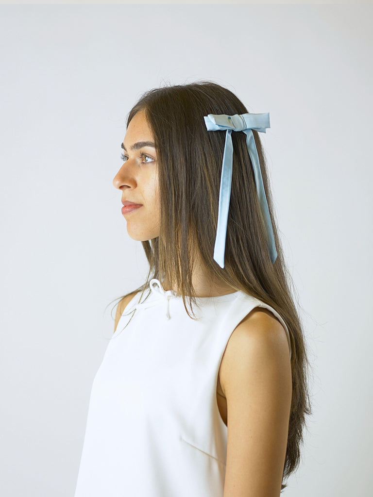 model in side profile wears an ivory sleeveless dress and a blue satin hair bow clip