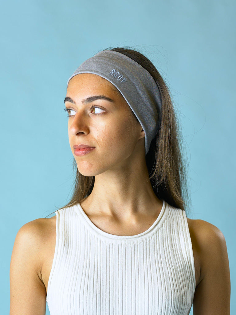 Woman wearing a grey stretch headband with a ROOP logo against a light blue background