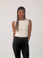 Woman wearing a white sleeveless top and black pants against a plain background. She wears a black stretch headband.