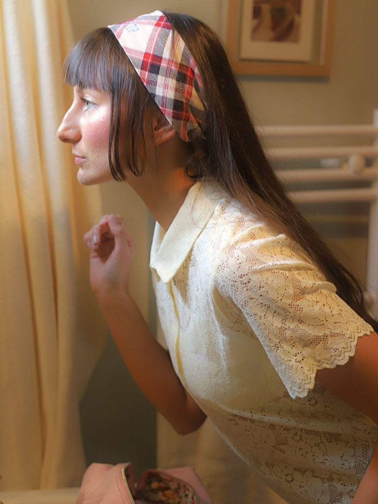 Woman wearing a plaid stretch headband and lace blouse in a softly lit bathroom.