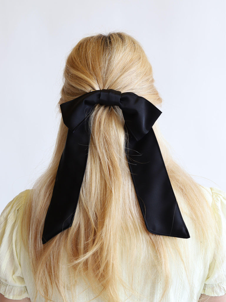 Black satin hair clip bow in blonde hair on a white background