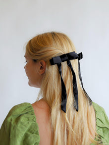 Person with long blonde hair wearing a black hair satin hair clips against a white background