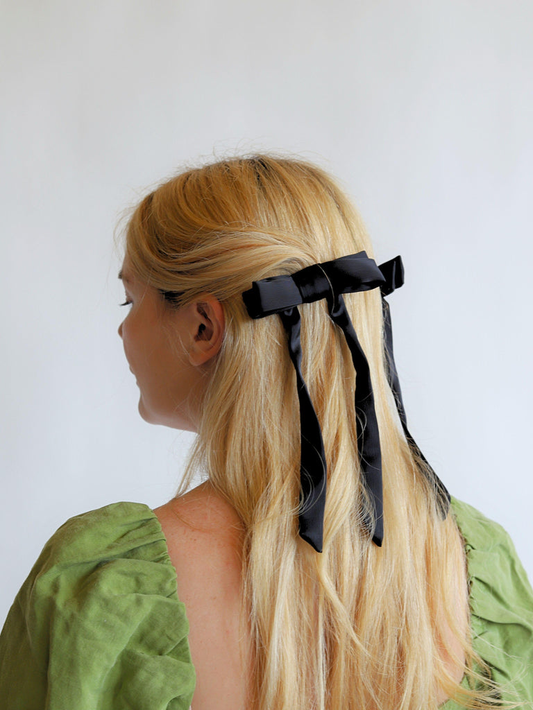 Person with long blonde hair wearing a black hair satin hair clips against a white background