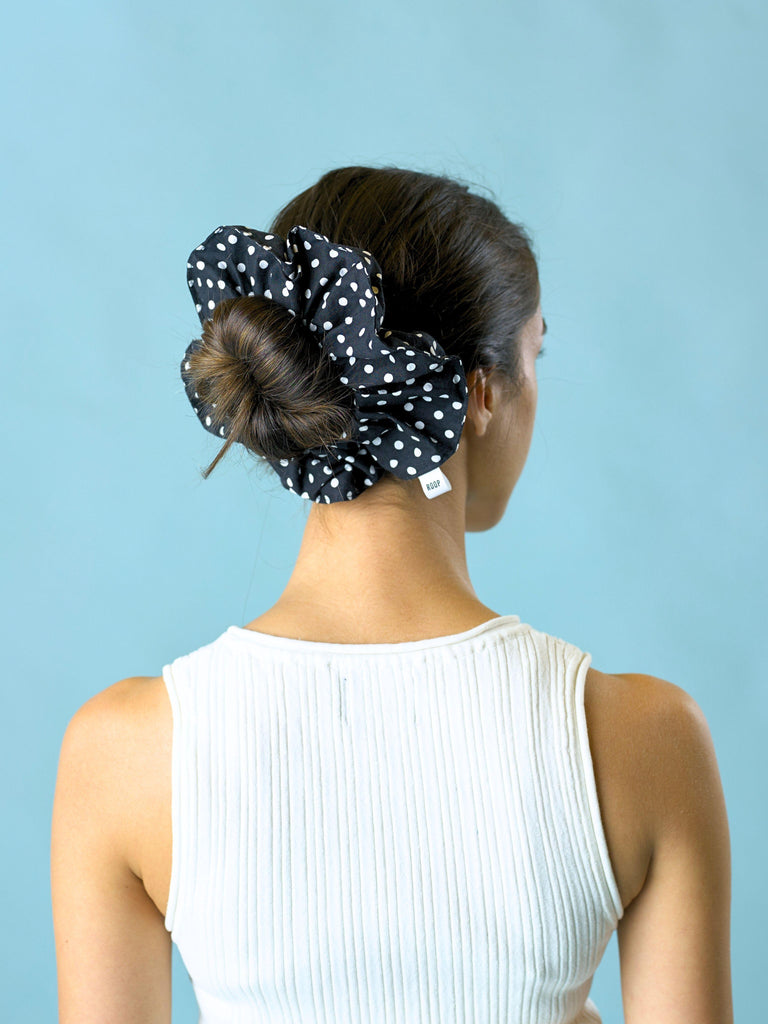 Person wearing a black polka dot scrunchie on a light blue background