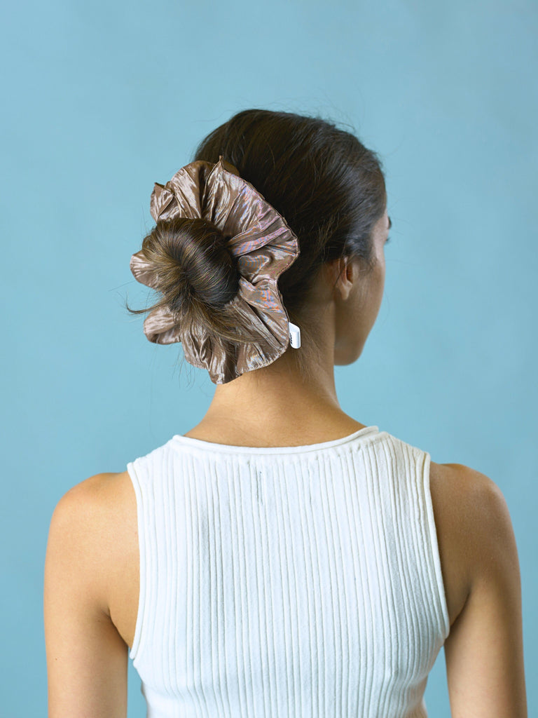 Woman with a brown crinkle taffeta scrunchie in her hair worn over her bun, set against a light blue background