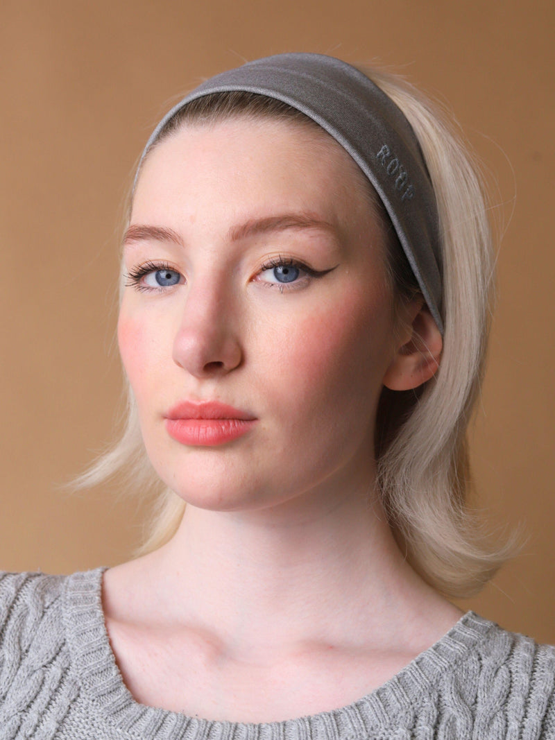 Woman wearing a grey stretch headband with ROOP logo on a beige background