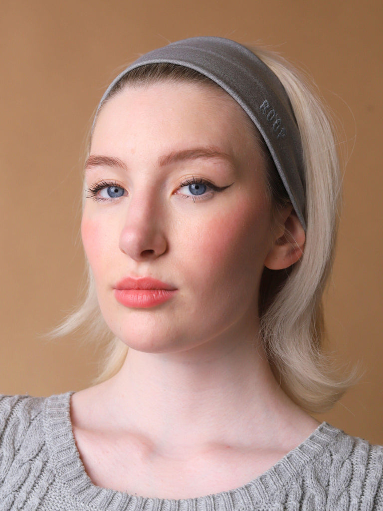Woman wearing a grey stretch headband with ROOP logo on a beige background