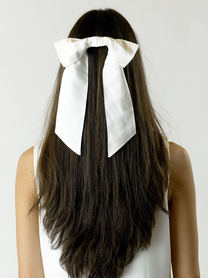 Person with long brown hair wearing a large ivory bamboo silk satin bow hair clip on a plain background