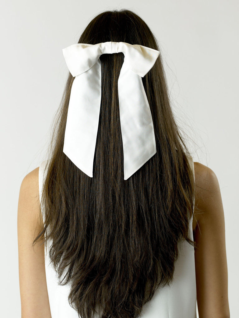 Person with long brown hair wearing a large ivory bamboo silk satin bow hair clip on a plain background