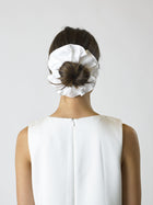 Person wearing a white sleeveless dress facing away wears an ivory bamboo silk satin scrunchie over their bun, set on a white background.