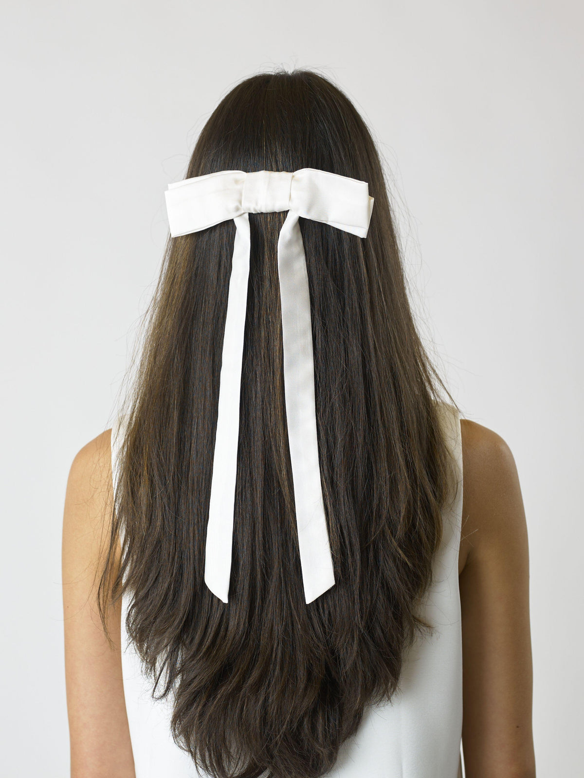 Person with long brown hair wearing an ivory bamboo silk satin bow hair clip on a white background on a plain background