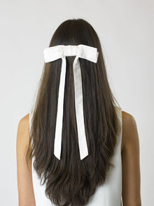 Person with long brown hair wearing an ivory bamboo silk satin bow hair clip on a white background on a plain background