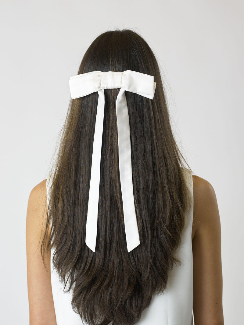 Person with long brown hair wearing an ivory bamboo silk satin bow hair clip on a white background on a plain background