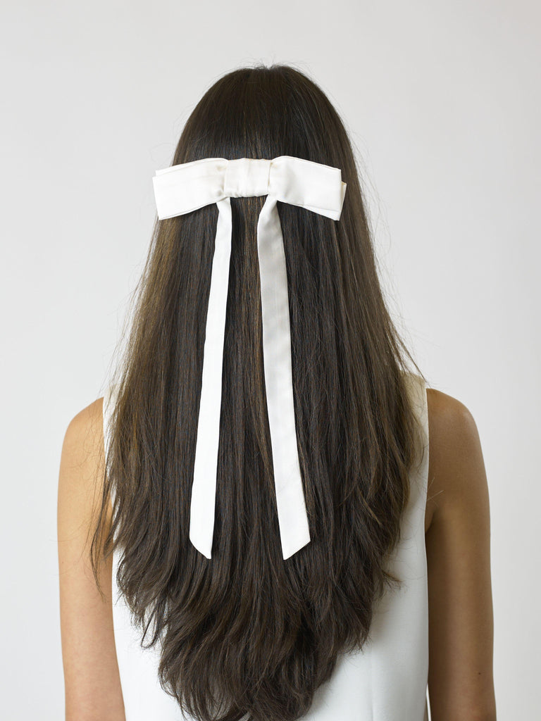 Person with long brown hair wearing an ivory bamboo silk satin bow hair clip on a white background on a plain background