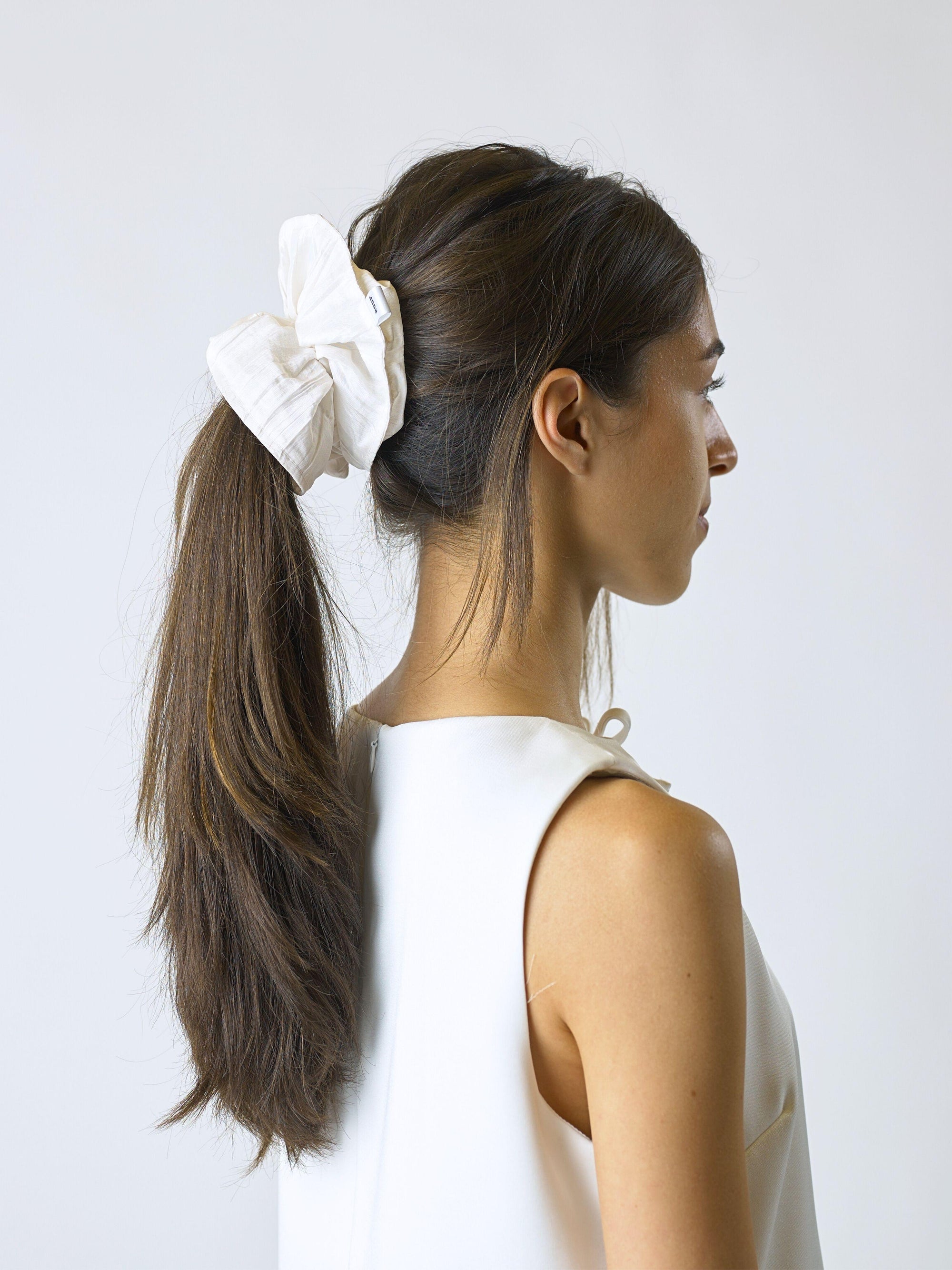 Woman with long brown hair tied back with an ivory crinkle taffeta scrunchie on a plain background