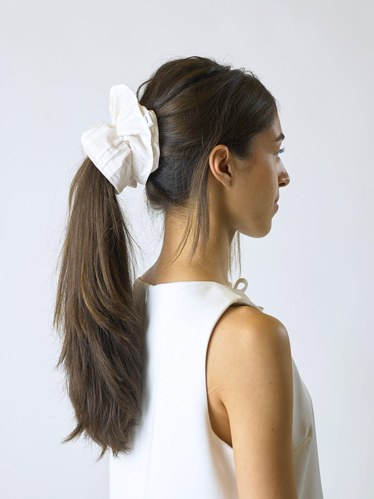 Woman with long brown hair tied back with an ivory crinkle taffeta scrunchie on a plain background