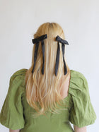 Person with long blonde hair wearing a pair of black satin hair bows on a white background