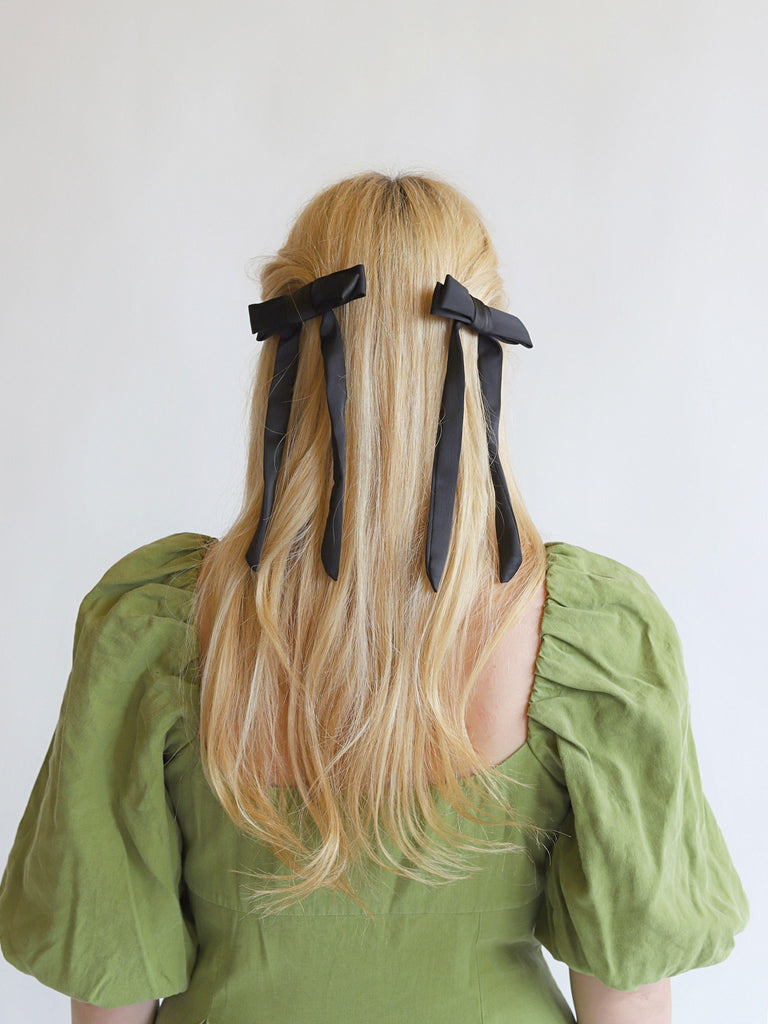Person with long blonde hair wearing a pair of black satin hair bows on a white background