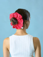 Woman wearing a pink taffeta scrunchie on a blue background