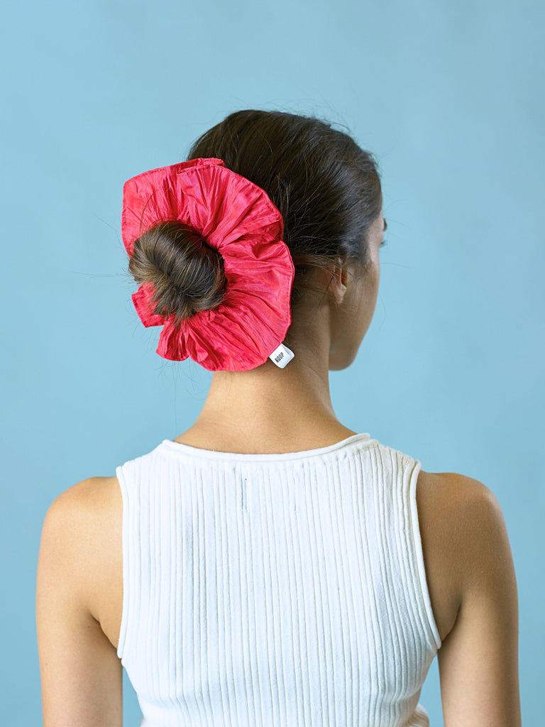 Woman wearing a pink taffeta scrunchie on a blue background