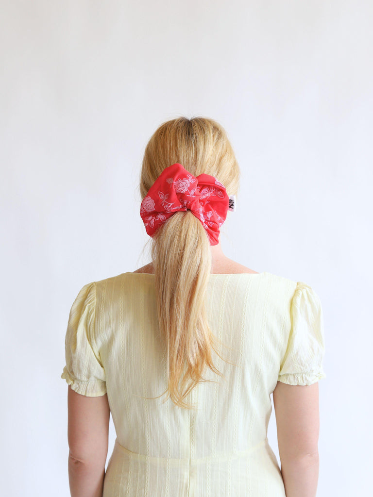 Person with blonde hair wearing a red rose print mesh scrunchie against a white background
