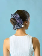 Woman wears a slate grey crinkle taffeta in her hair over her bun, set against a light blue background