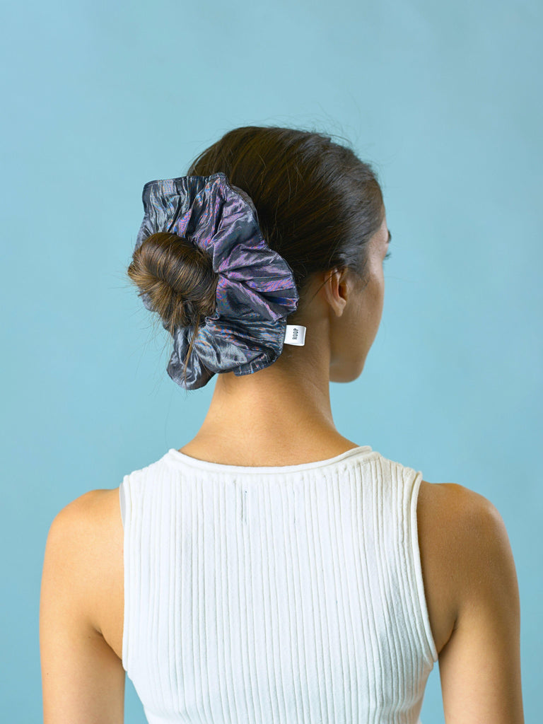 Woman wears a slate grey crinkle taffeta in her hair over her bun, set against a light blue background