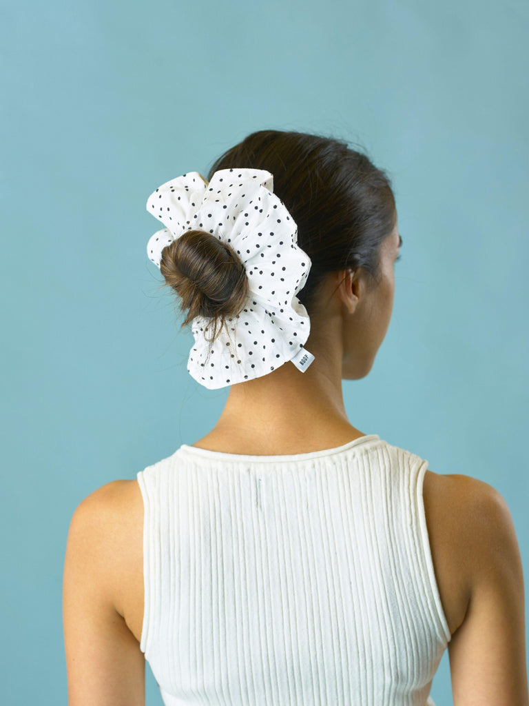 Woman with a white and black polka dot scrunchie in her hair against a light blue background