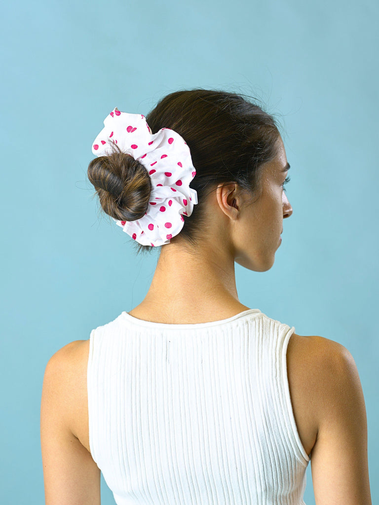 Woman with a bun wearing a white and pink polka dot scrunchie against a blue background