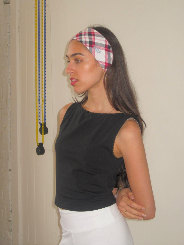 Woman wearing a black sleeveless top and plaid headband against a neutral wall.
