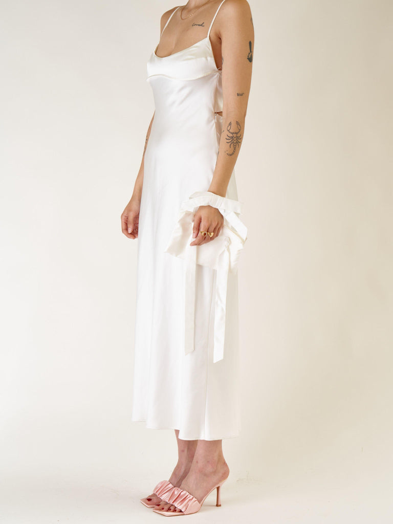 Woman wearing an ivory slip dress with an ivory bamboo silk satin wristlet bracelet bridal bag on a plain background
