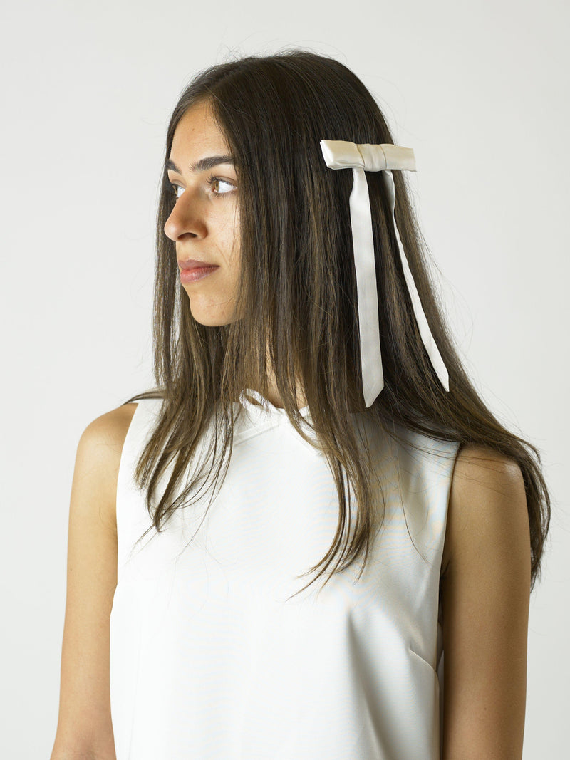 Woman with brown hair wearing an ivory bamboo silk satin hair bow clip on a plain background