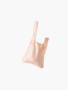 Peach satin knot bag against a plain white background. The elegant bag has a twisted handle and sleek, glossy fabric, exuding a chic, minimalist style.