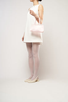 A model wearing a bridal white mini dress, holding a pink satin handbag.