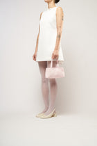 A model wearing a bridal white mini dress, holding a pink satin handbag.