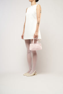 A model wearing a bridal white mini dress, holding a pink satin handbag.